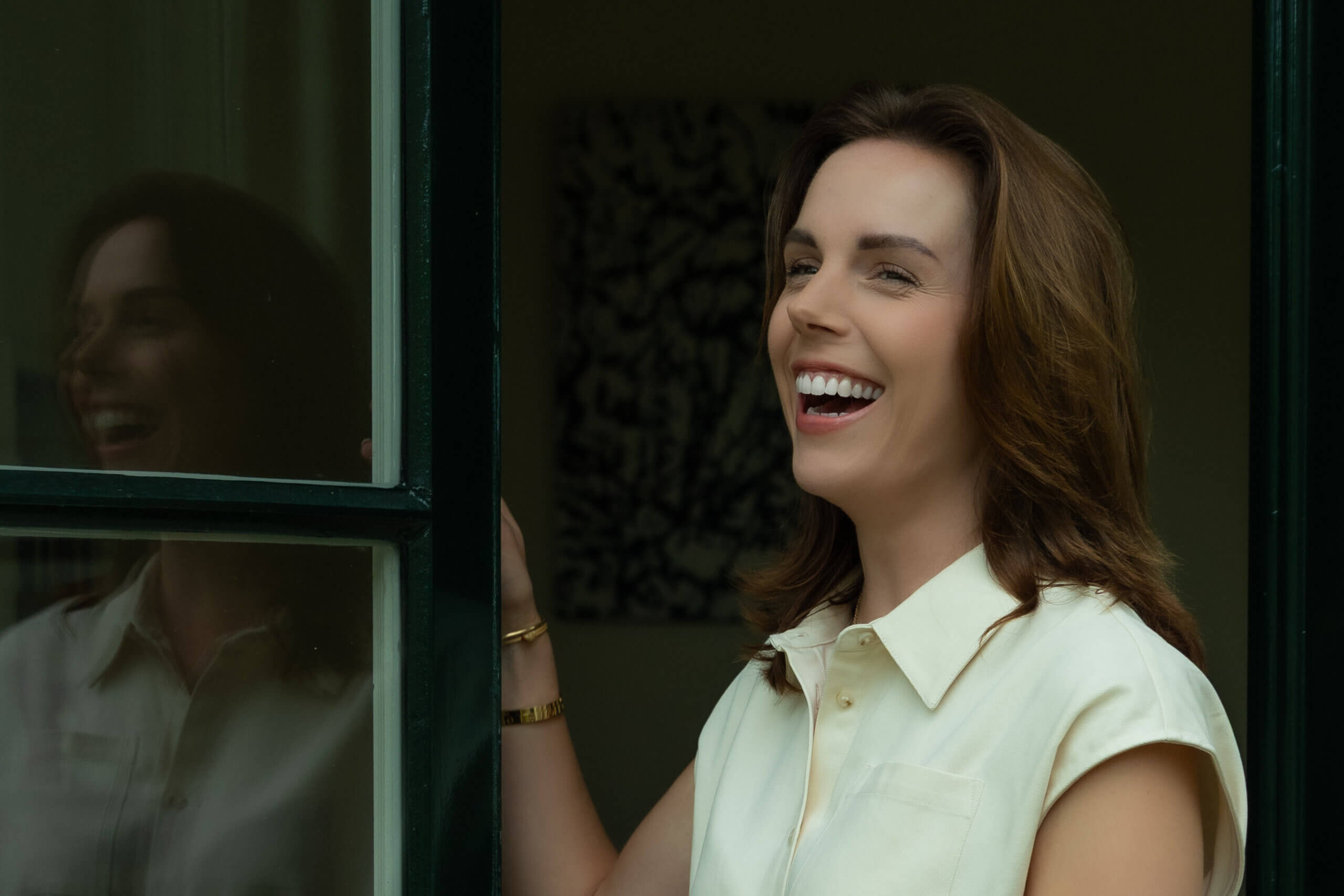 Vrouw in werkomgeving, ontspannen moment bij het raam, met een natuurlijke en menselijke uitstraling.